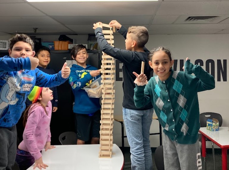 Children cheering on a boy building a tall block structure