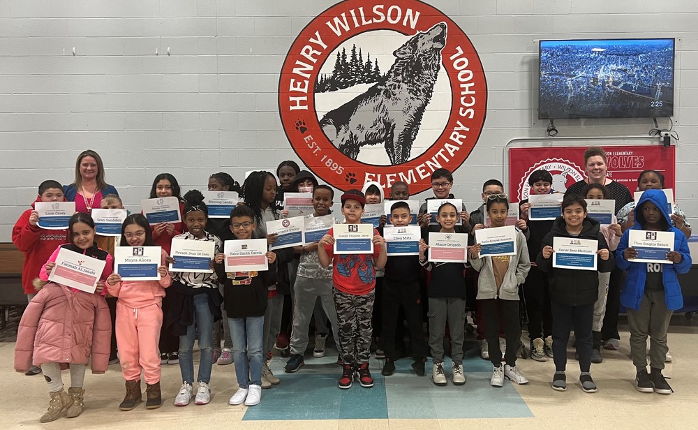Children lined up holding their certificates in front of the Wilson logo