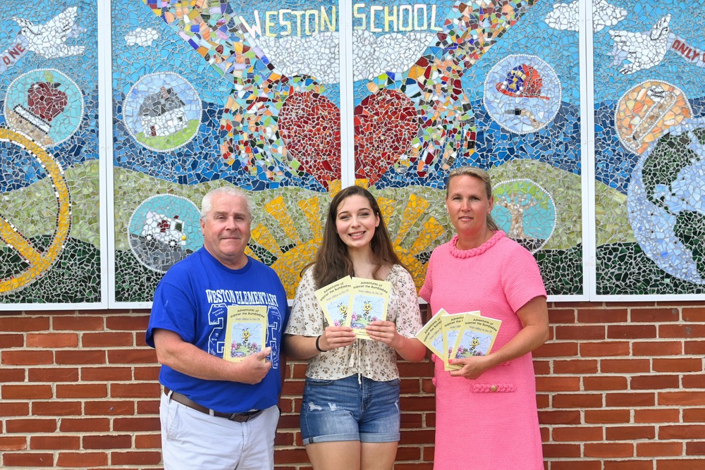 Weston Assistant Principal Rick Chretien, illustrator Ana Liz Bourassa and Superintendent of Schools Jennifer Gillis pose for a photo outside Weston with copies of a book Bourassa illustrated